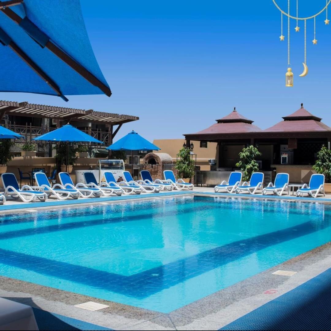 Safir Hotel Cairo Giza Exterior foto The photo showcases a bright, inviting swimming pool surrounded by lounging chairs. The pool is set in a sunny outdoor area, with clear blue water reflecting the sky. There are several blue umbrellas providing shade over the lounge chairs, which are 