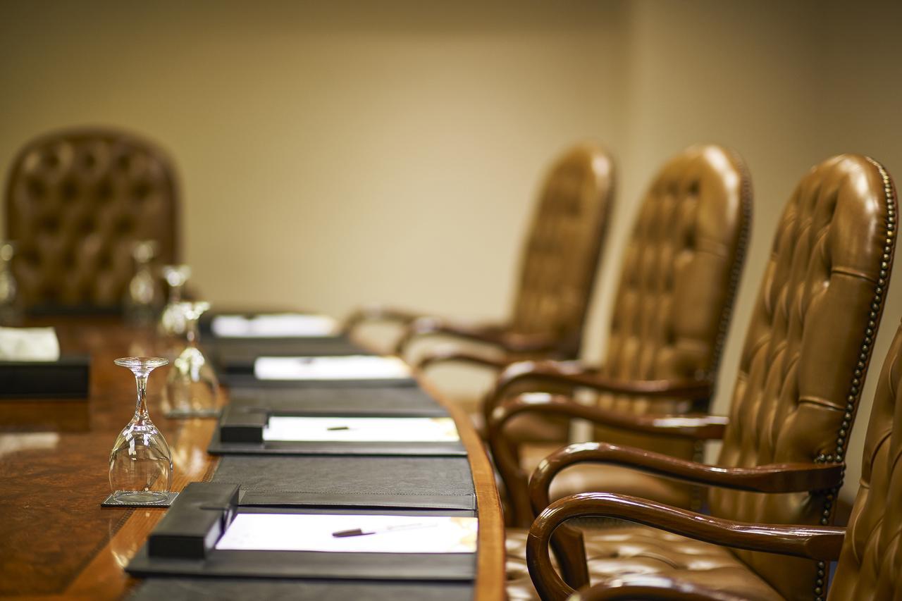 Safir Hotel Cairo Giza Exterior foto The photo shows a conference room setting with a long wooden table and several high-backed chairs. The chairs appear to be upholstered in a brown leather material. Each place at the table has a black folder or pad, and there are also glass water gobl