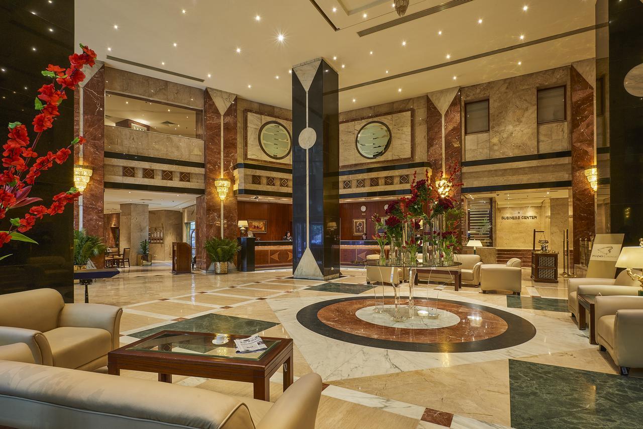 Safir Hotel Cairo Giza Exterior foto The photo shows a luxurious hotel lobby. The space features elegant marble flooring with a circular design at the center. There are comfortable seating arrangements with light-colored sofas and wooden coffee tables. Lush green plants and vibrant flor