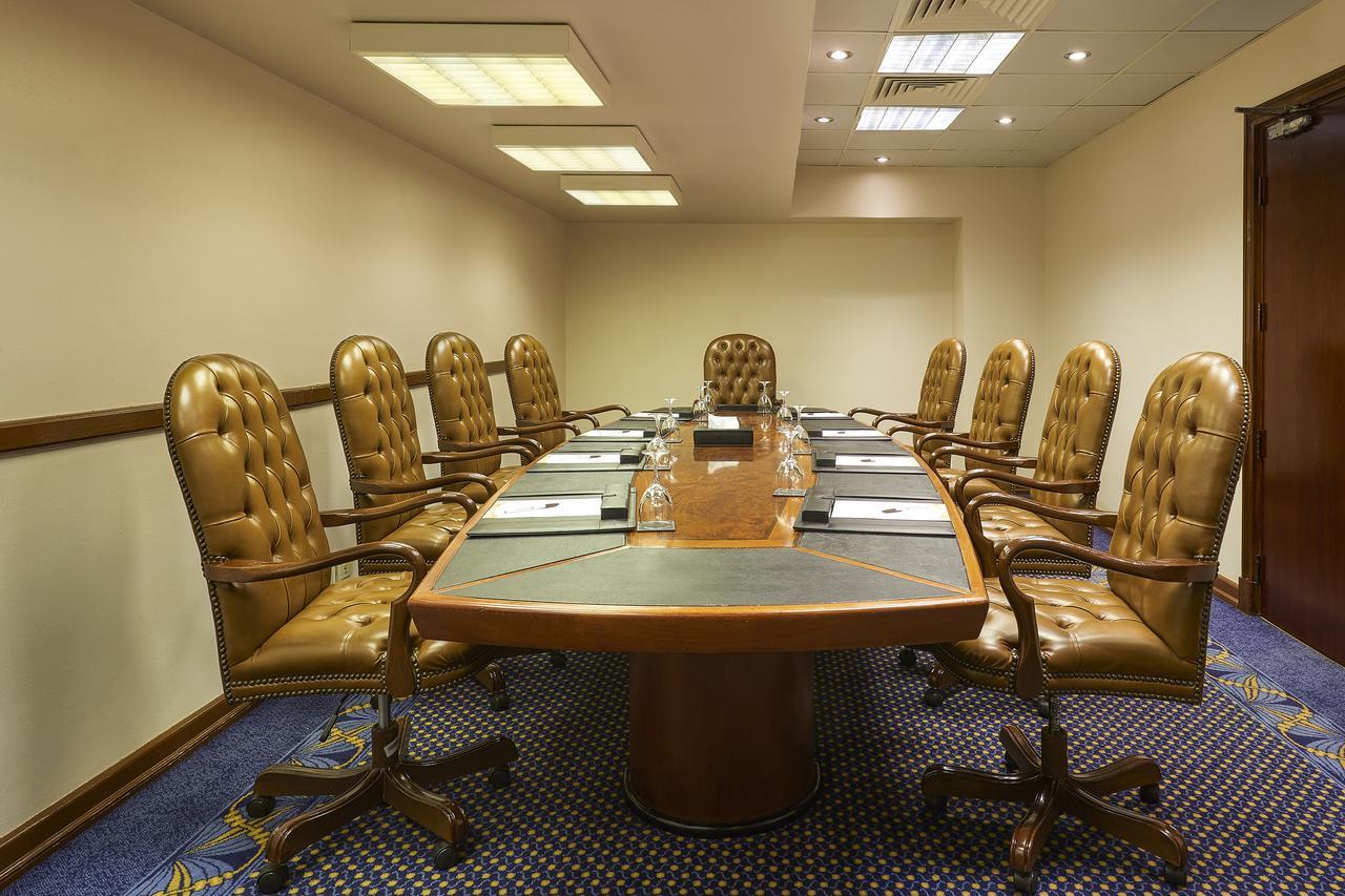 Safir Hotel Cairo Giza Exterior foto The photo shows a conference room with a large oval table surrounded by several brown leather chairs. There are eight chairs in total, each with a high back and wheels. The table has some notepads and glasses of water set up on it. The room has neutr