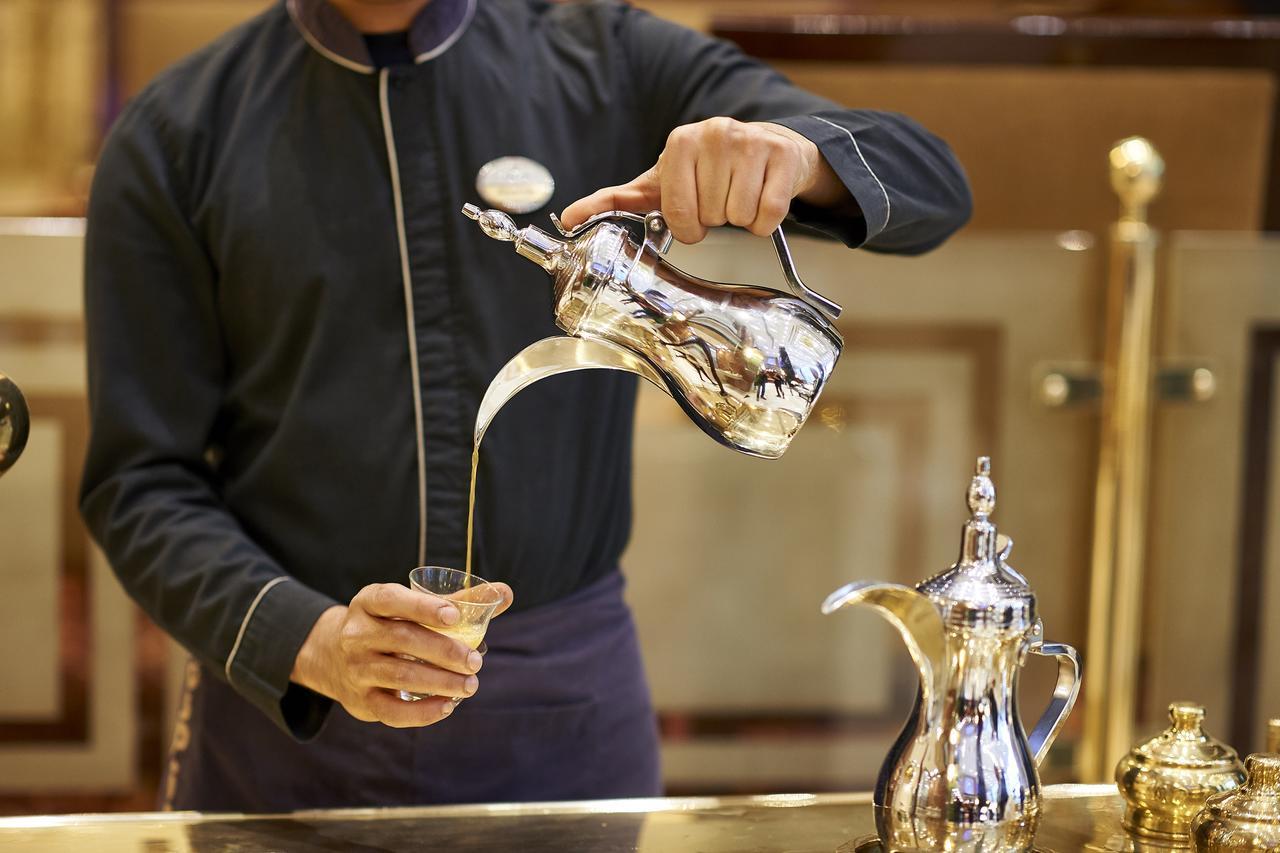 Safir Hotel Cairo Giza Exterior foto The image shows a server pouring a beverage from a shiny silver teapot into a glass. The server is wearing a dark uniform and has a focused expression. The teapot is intricately designed, and there is another similar pot alongside it on the counter. 