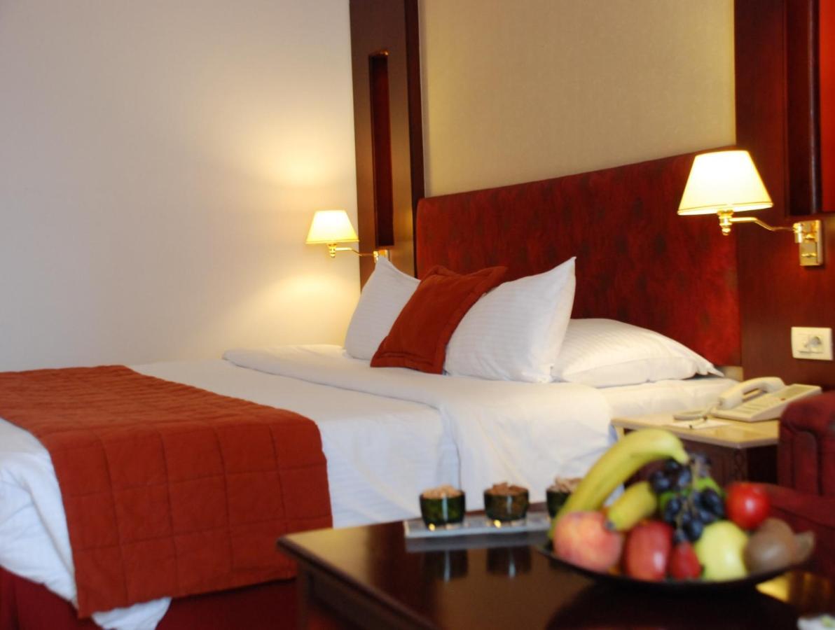 Safir Hotel Cairo Giza Zimmer foto The photo shows the interior of a hotel room featuring two beds with white bedding and an orange throw blanket. There are decorative pillows on the beds. The walls are designed in warm tones, and there are two bedside lamps providing soft illuminatio